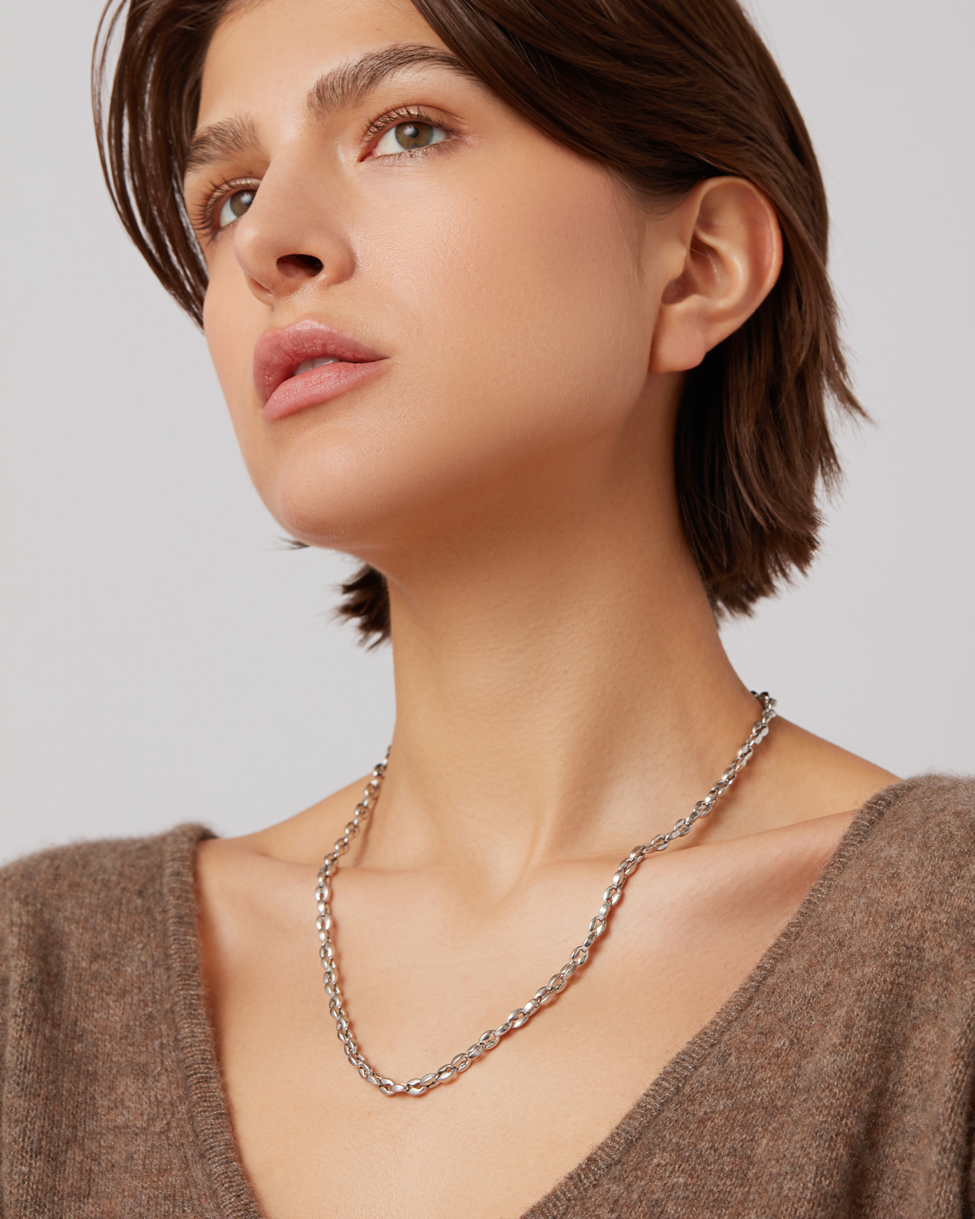 Portrait of a woman with braided hair, silver earrings, and a beige top.